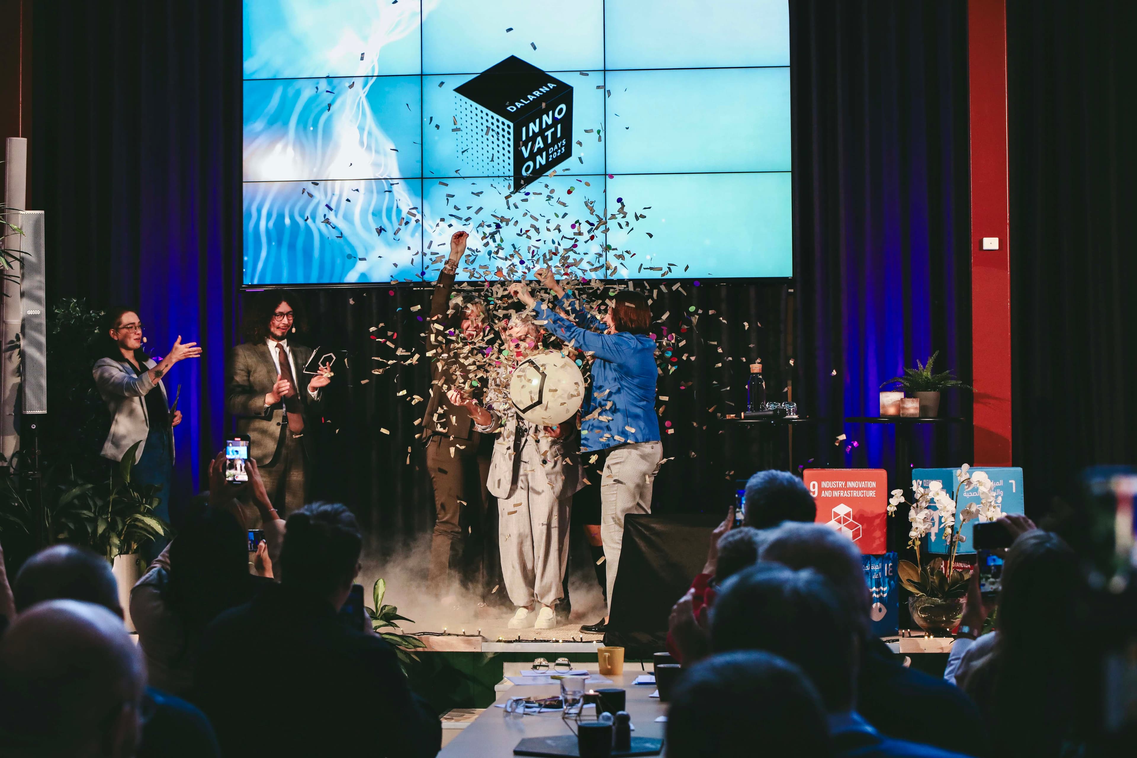 people celebrating on stage. confetti falling and a screen with the text Dalarna innovation days 2022