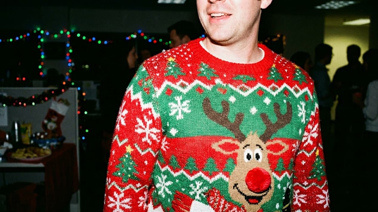 a man wearing a knitted christmas sweater in red and green with a cartoon reindeer on it