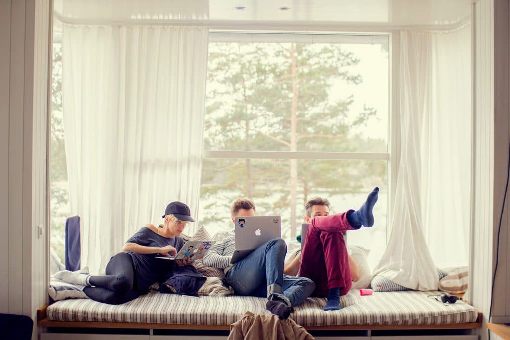 three people sitting in a sofa by the window working on their laptops